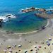 Pessoas aproveitando praia com guarda-sóis coloridos e mar calmo na cidade litorânea