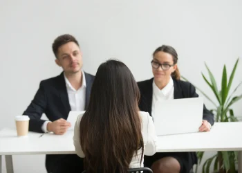 Candidato participando de entrevista de emprego com dois recrutadores em ambiente corporativo.