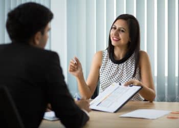 Candidata conversando com recrutador durante entrevista de emprego, segurando currículo e demonstrando confiança e autenticidade