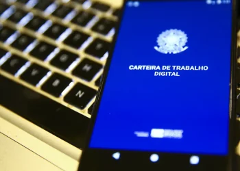 Smartphone exibindo a tela inicial do aplicativo Carteira de Trabalho Digital sobre teclado de notebook, representando o mercado de trabalho em 2026