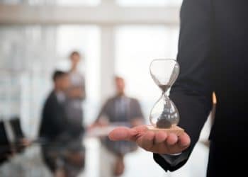 Escala 6x1: executivo segura ampulheta em reunião corporativa, simbolizando o debate sobre jornada de trabalho