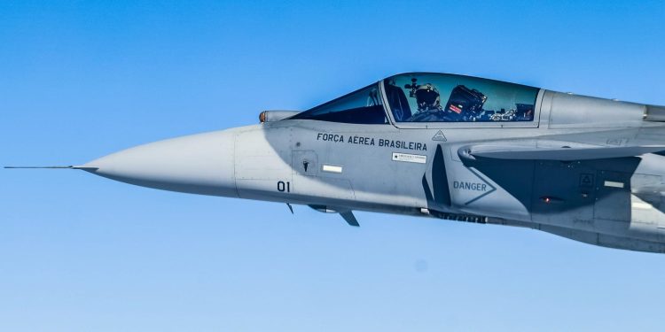 Piloto dentro de caça supersônico da Força Aérea Brasileira em voo sob céu azul