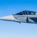 Piloto dentro de caça supersônico da Força Aérea Brasileira em voo sob céu azul