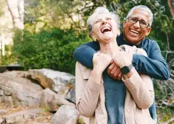 Casal de idosos sorrindo e se abraçando durante um passeio ao ar livre, representando felicidade e bem-estar na terceira idade.