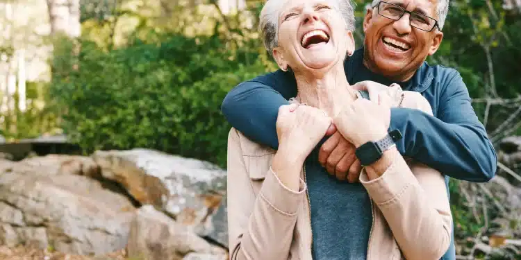 Casal de idosos sorrindo e se abraçando durante um passeio ao ar livre, representando felicidade e bem-estar na terceira idade.