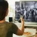 Mulher assistindo a filme sobre a Revolução Industrial, com foco em trabalhadores operando máquinas.