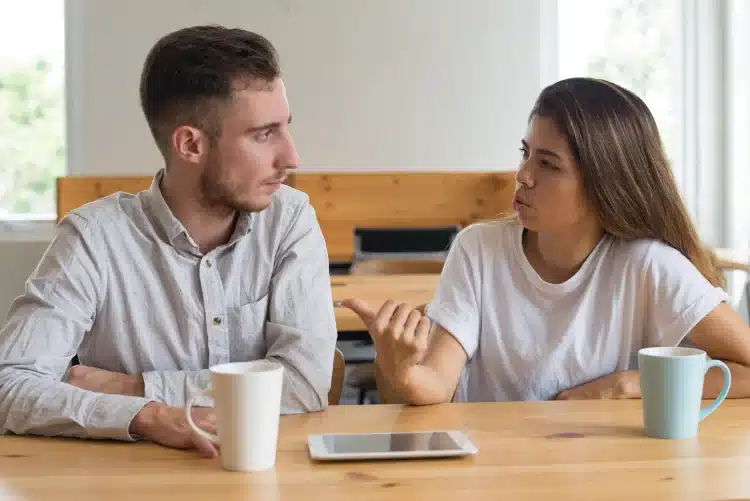 Dois jovens conversam seriamente em uma mesa, demonstrando escuta ativa e empatia