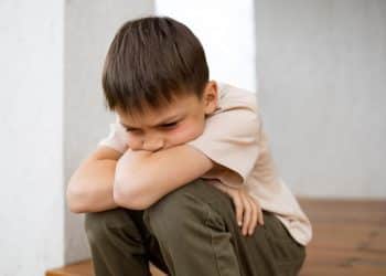 Menino triste sentado, refletindo sobre o impacto das palavras no desenvolvimento emocional infantil.