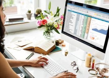 Mulher trabalhando no computador com planilha do Excel aberta exibindo gráficos e dados financeiros.