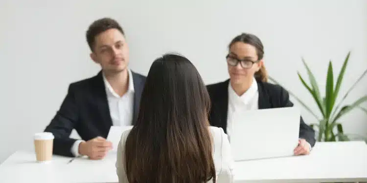 Candidata de costas sendo entrevistada por dois recrutadores em ambiente corporativo, representando o momento da entrevista de emprego para o qual a Inteligência Artificial pode ajudar na preparação