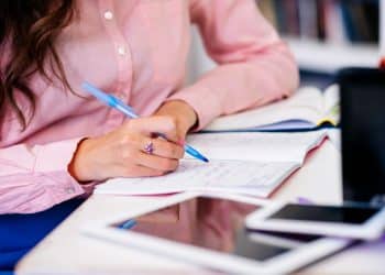 Concurso Senador Canedo GO: mãos anotando em caderno com caneta azul e materiais de estudo sobre a mesa