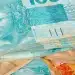 Notas de dinheiro coloridas com destaque para a cédula de 100 reais em azul, representando o tema de pagamentos de março do INSS.