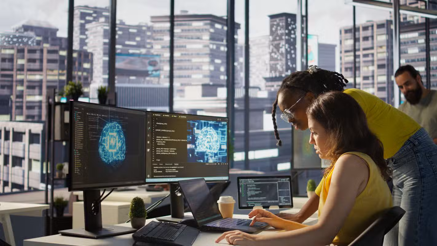 Duas profissionais analisando tela de computador com interface de Inteligência Artificial em ambiente de trabalho moderno, ilustrando o uso prático da IA como ferramenta de preparação para entrevistas de emprego