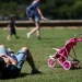 Projeto de licença-paternidade aguarda sanção de Lula — adulto deitado na grama de parque brincando com criança pequena ao lado de carrinho de bebê rosa