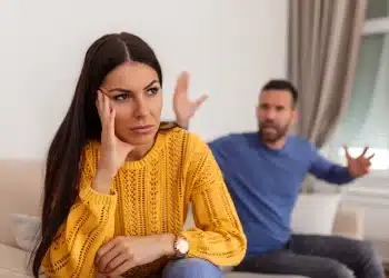 Imagem de um casal em uma discussão, com a mulher visivelmente desconfortável e o homem gesticulando em um ambiente doméstico, representando a dinâmica de um relacionamento abusivo, como o gaslighting.