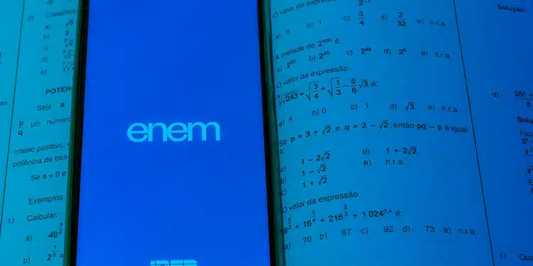 Smartphone exibindo tela do ENEM apoiado sobre livro aberto de matemática com questões