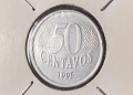 Close-up de uma moeda de 50 centavos de 1995 da primeira família do Real, protegida em um suporte para colecionador (coin holder).