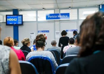 Pessoas sentadas em sala de espera de unidade do INSS aguardando atendimento de perícia médica