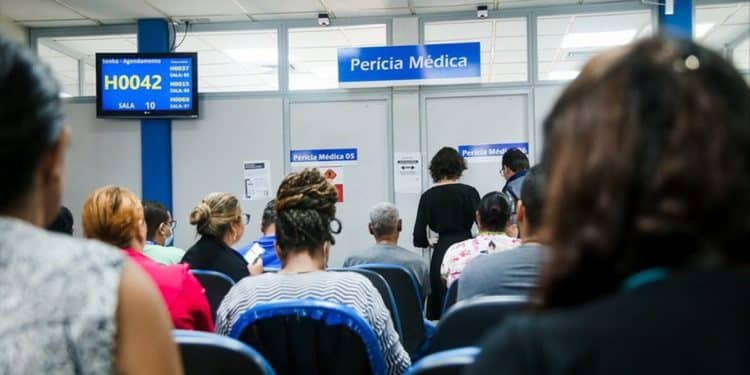 Pessoas sentadas em sala de espera de unidade do INSS aguardando atendimento de perícia médica