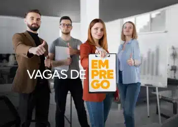 Quatro pessoas sorrindo, mostrando sinal de positivo e segurando placa com texto “Emprego” em escritório moderno