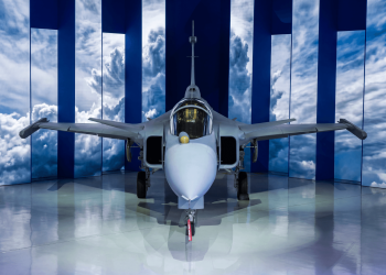 Avião caça supersônico cinza exposto em hangar moderno com fundo de céu azul