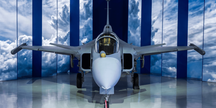 Avião caça supersônico cinza exposto em hangar moderno com fundo de céu azul