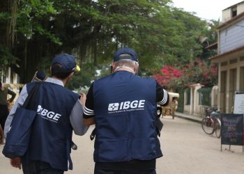 Dois agentes do IBGE de costas caminhando em área urbana durante trabalho de campo