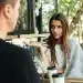 Mulher com expressão confusa e mão estendida, envolvida em um cobertor cinza, conversando com um homem de costas. Ela parece estar explicando algo ou reagindo a uma frase rude. A imagem ilustra uma conversa difícil.