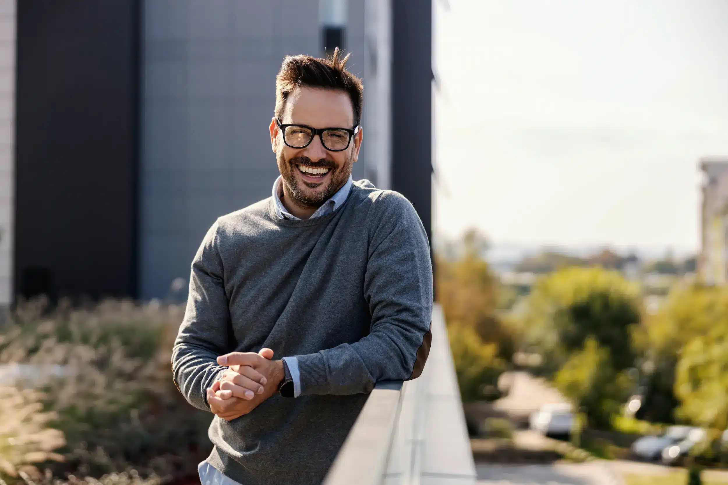 Homem sorridente, com óculos, em um ambiente ao ar livre, transmitindo confiança e positivismo.