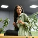 Mulher sorrindo com uma expressão confiante em ambiente de escritório, segurando óculos.
