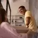 Homem negro de camiseta amarela sorri amplamente enquanto segura uma caixa ao lado de uma mulher de blusa rosa, em cena de leveza e conexão