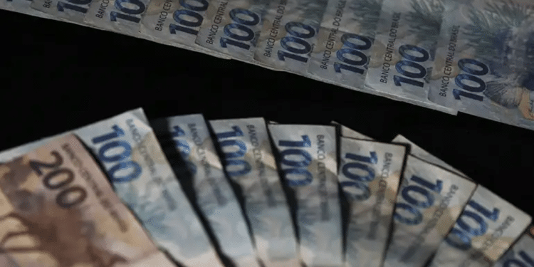 Cédulas de cem e duzentos reais do Banco Central do Brasil organizadas em leque sobre superfície escura com iluminação direcional