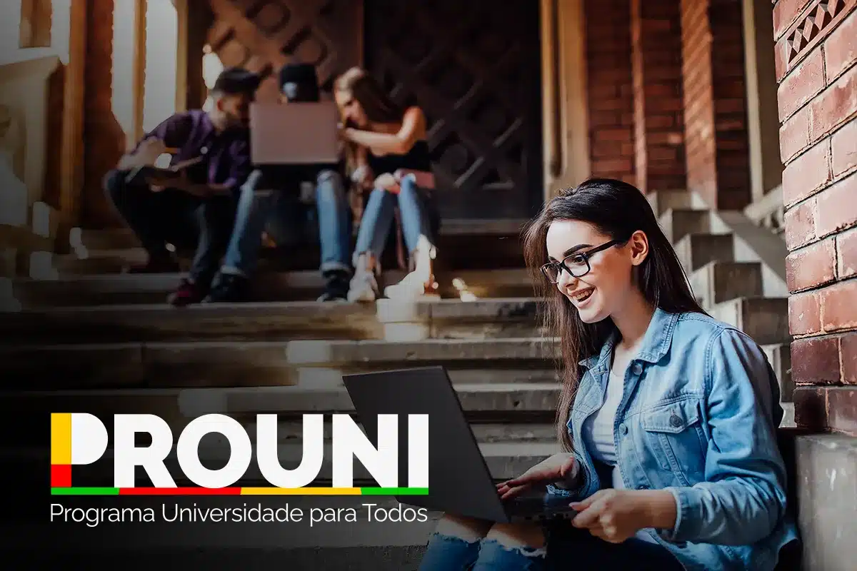 Estudante jovem usando óculos e jaqueta jeans sentada em uma escadaria, sorrindo enquanto utiliza um laptop. Ao fundo, outros estudantes conversam. No canto inferior esquerdo, o logotipo colorido do Prouni (Programa Universidade para Todos).