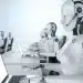 Robôs humanoides com fones de ouvido trabalhando em notebooks em ambiente de escritório, ilustrando o debate sobre automação, inteligência artificial e o futuro das profissões no mercado de trabalho.