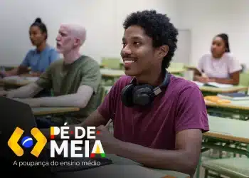 Jovem estudante negro sorrindo em sala de aula com fone de ouvido no pescoço e notebook à frente, com a logo do Pé-de-Meia — A poupança do ensino médio — no canto inferior, representando o início da jornada financeira de quem participa do programa