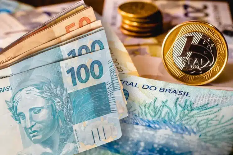 Notas de 100 e 50 reais junto a moedas de 1 real sobre superfície