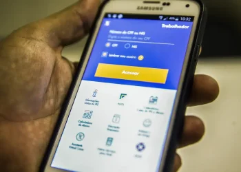 Mão segurando smartphone Samsung com aplicativo do trabalhador aberto, mostrando tela de acesso ao FGTS com campo para CPF ou NIS