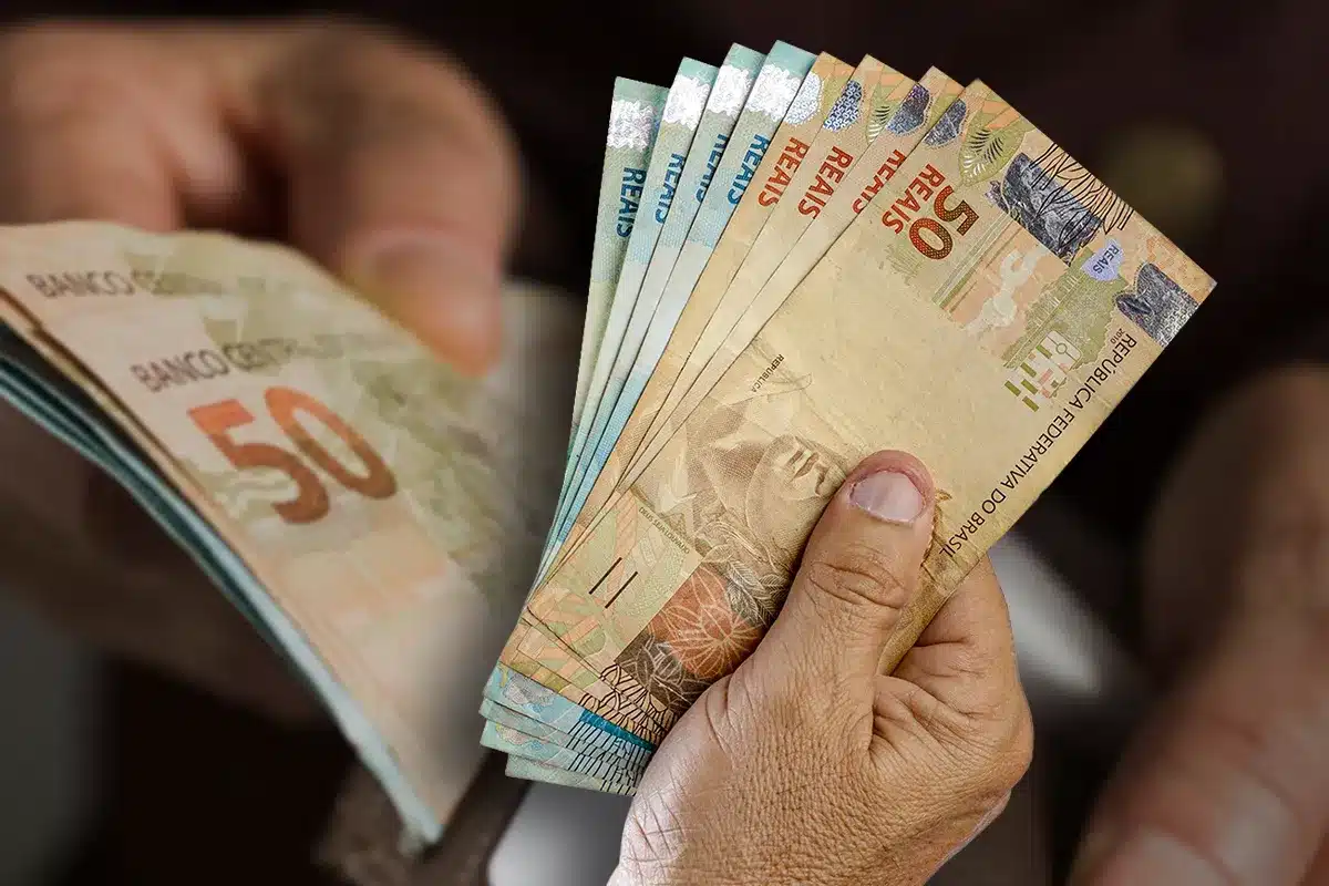 Trabalhador segurando notas de R$ 50,00, ilustrando o Saque Calamidade do FGTS, liberado após desastres naturais.