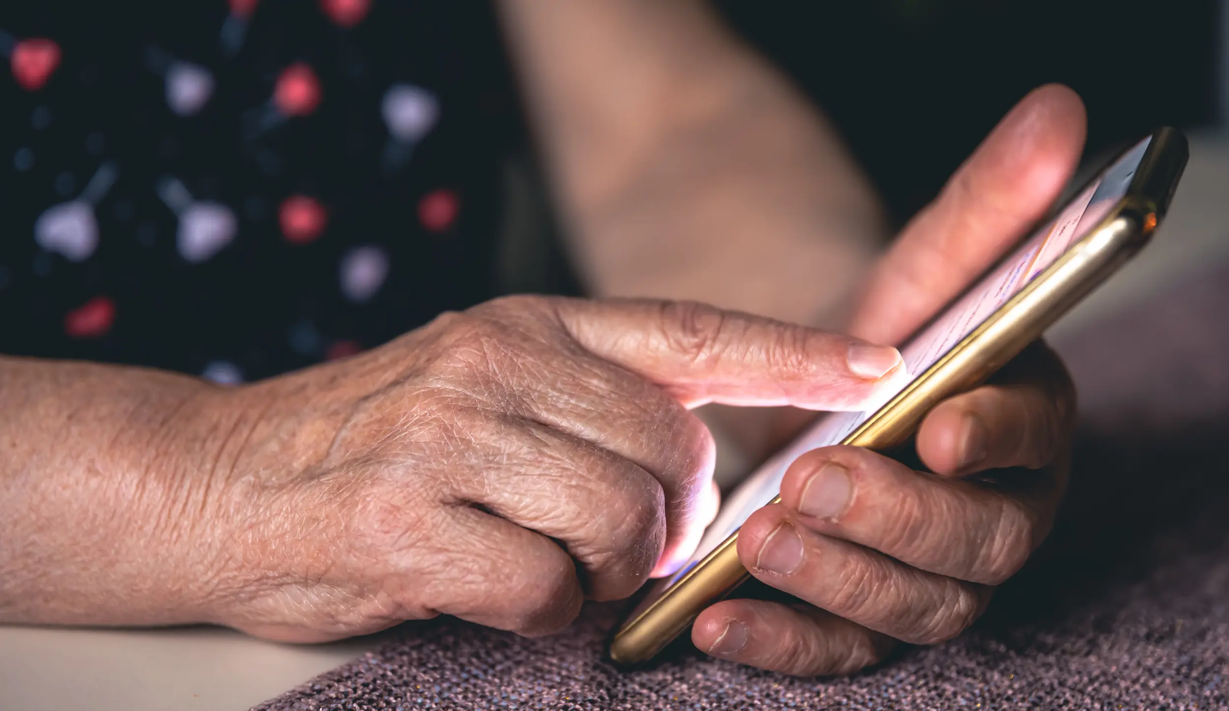 Mãos de uma pessoa idosa utilizando um smartphone, ilustrando cuidados com segurança digital e prevenção de golpes virtuais.