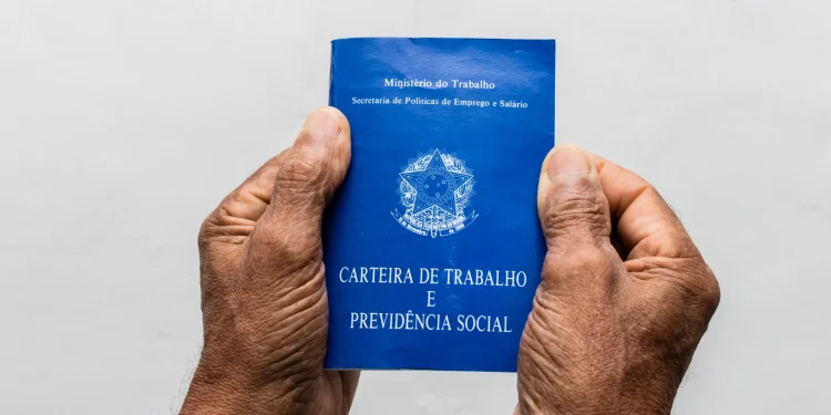 Duas mãos seguram uma carteira de trabalho azul em fundo claro