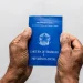Duas mãos seguram uma carteira de trabalho azul em fundo claro