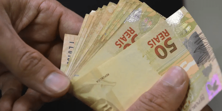 Mãos segurando diversas cédulas de cinquenta reais em close representando os novos valores do 13º salário do INSS que podem chegar a R$ 8.475,55 em 2026