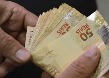 13º salário do INSS: mãos segurando notas de cinquenta reais representando o montante liberado pelo benefício
