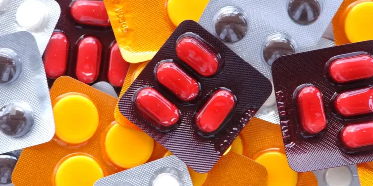 Diversas cartelas de medicamentos coloridas — vermelhas, amarelas e cinzas — espalhadas, ilustrando a nova lei brasileira que permite a instalação de farmácias e drogarias dentro de supermercados