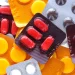 Diversas cartelas de medicamentos coloridas — vermelhas, amarelas e cinzas — espalhadas, ilustrando a nova lei brasileira que permite a instalação de farmácias e drogarias dentro de supermercados