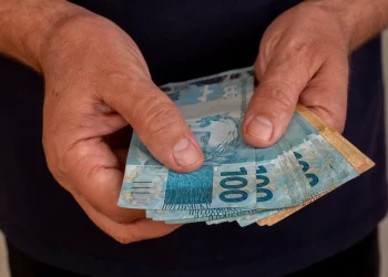 Aposentado segurando notas de real referente ao pagamento da segunda parcela do 13º do INSS.