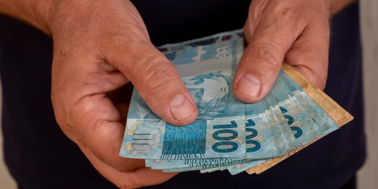 Aposentado segurando notas de real referente ao pagamento da segunda parcela do 13º do INSS.