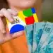 Cartão do Bolsa Família 2026 em mãos, com notas de R$ 100 ao fundo.