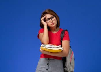 Estudante cansada segura livros e cadernos com expressão de estresse, simbolizando o atraso no pagamento de R$ 1.000 do Pé-de-Meia.