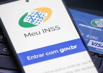 Celular com a tela do aplicativo Meu INSS aberta ao lado de cartão da Previdência Social sobre teclado de notebook